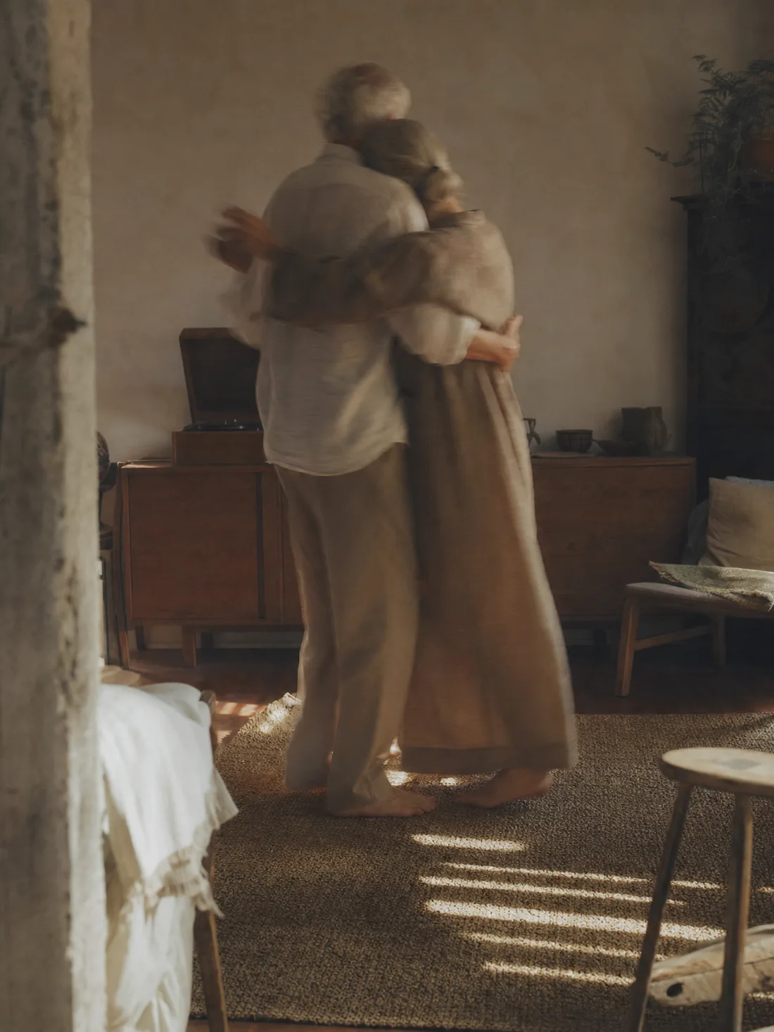 An older couple slow-dancing in a living room, seen from behind